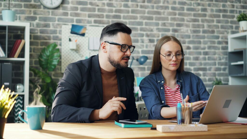 A man and woman collaborating on a project using a laptop at an office desk.